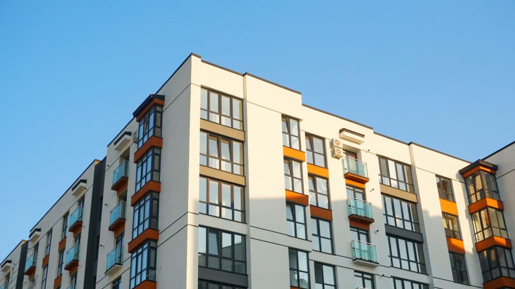 Modern mid-rise multifamily apartment building with large windows and private balconies, designed for high-density urban living.
