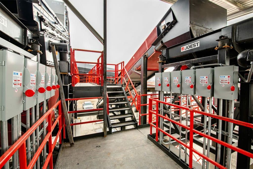 Industrial conveyor system at Metro Recycling, featuring black and red structures, control panels, and walkways.
