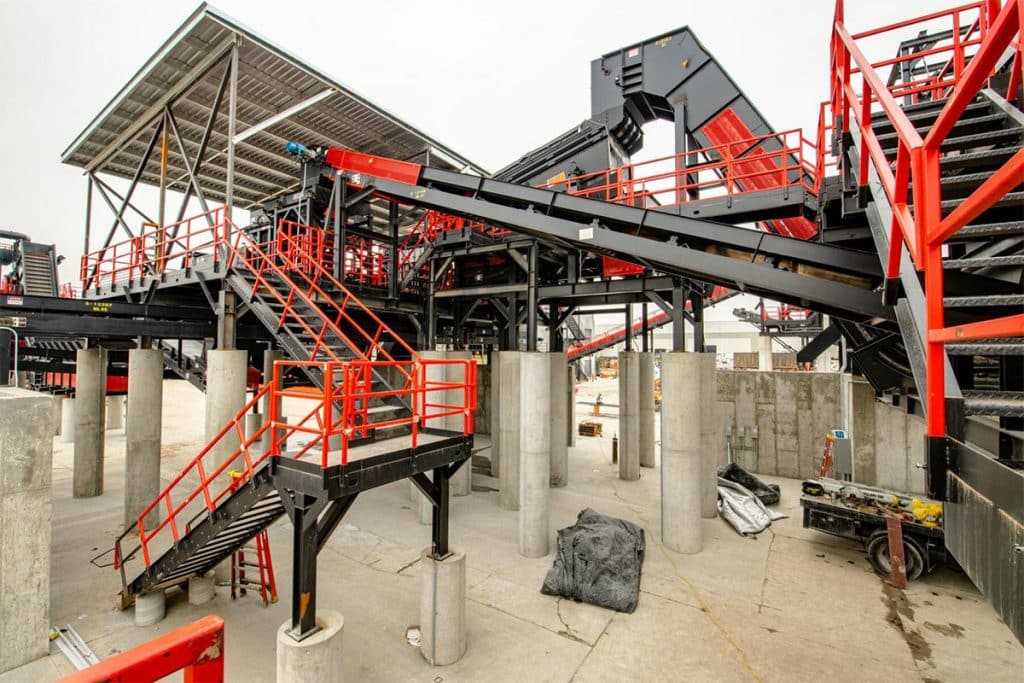 Large industrial conveyor system at Metro Recycling with red railings, metal walkways, and concrete support columns.