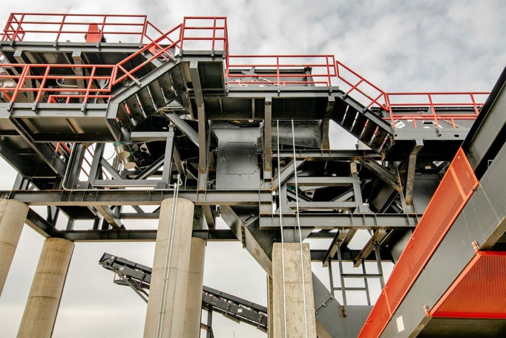 Metro Recycling's elevated conveyor system with steel framing, red safety railings, and concrete support columns.