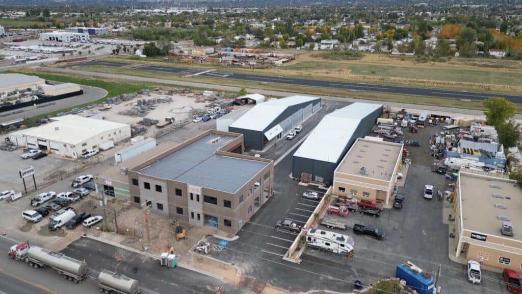 Aerial view of an industrial construction site featuring multiple newly built warehouses, office buildings, and parking areas, with a nearby runway and surrounding infrastructure.